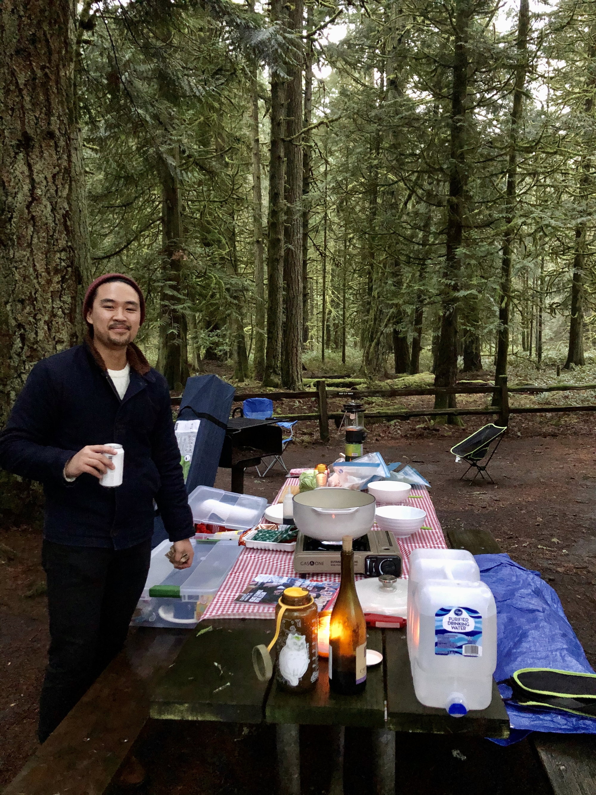 Man next to a campground picnic table with a portable burner and soup ingredients