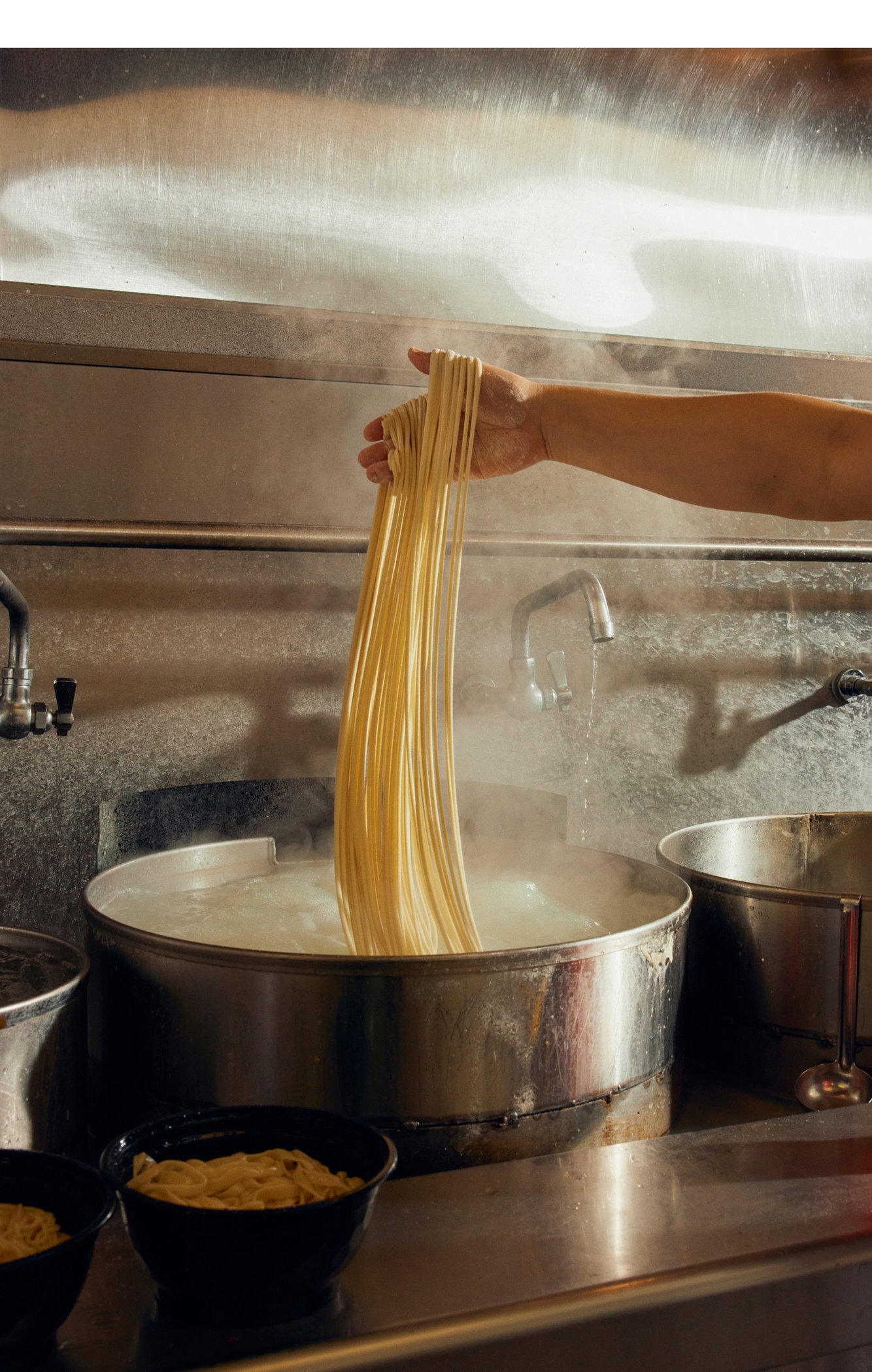 A hand drops freshly hand-pulled noodles in a pot of boiling water.