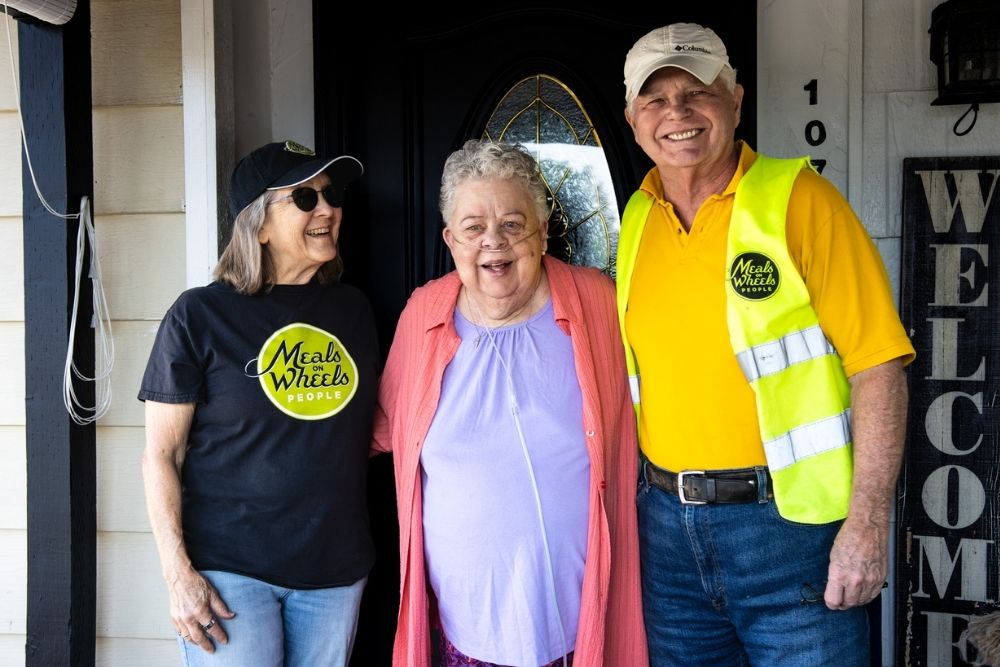 Meals on Wheels People volunteers Sally and Chris Galligan have delivered meals to Sheena since 2023. Their visits bring more than food — they’ve built a friendship Sheena describes as “like family.” Photo by Nicole Ceron.